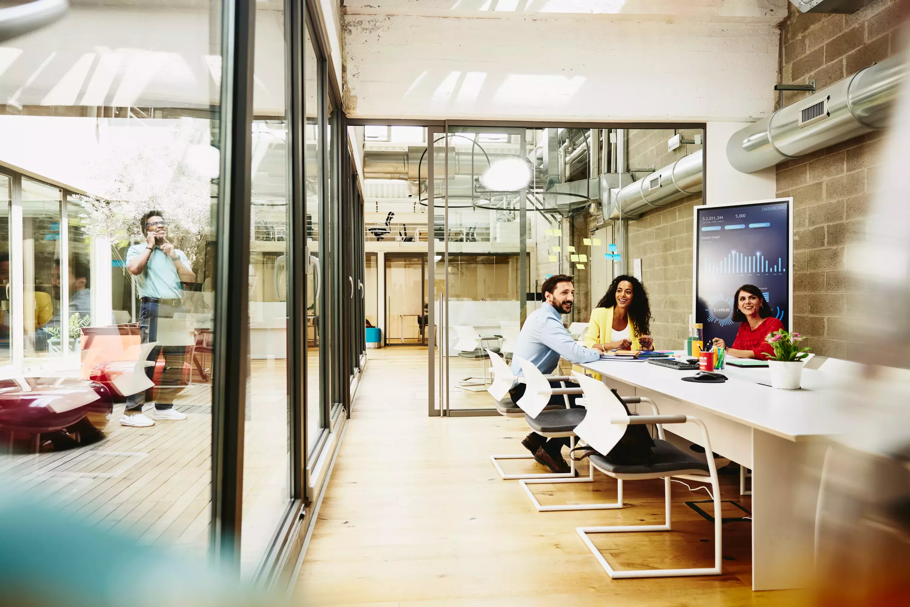 Three colleagues having a meeting in a meeting room, while one colleague is making a call outside the room.
