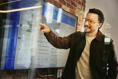 Male standing in front of a screen and pointing at data.