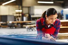 Womale wearing a red overall writing on a paper in a production site/factory.
