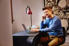 Male in a blue shirt sitting at a desk working on his laptop