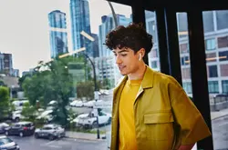 Male in yellow shirt, width earphones, standing at a window looking down