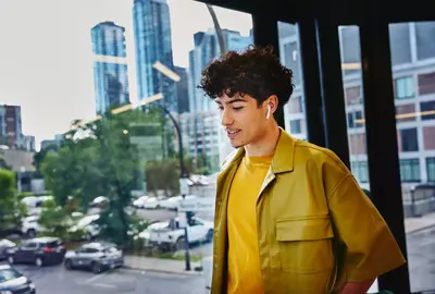 Male in yellow shirt, width earphones, standing at a window looking down