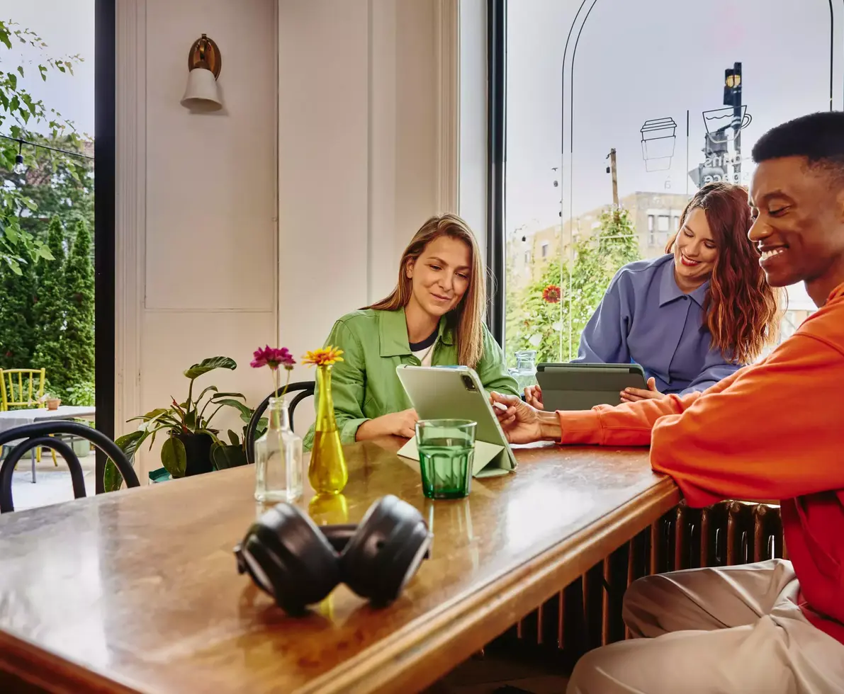 Two females and male sitting on a table in cafe working on tablets