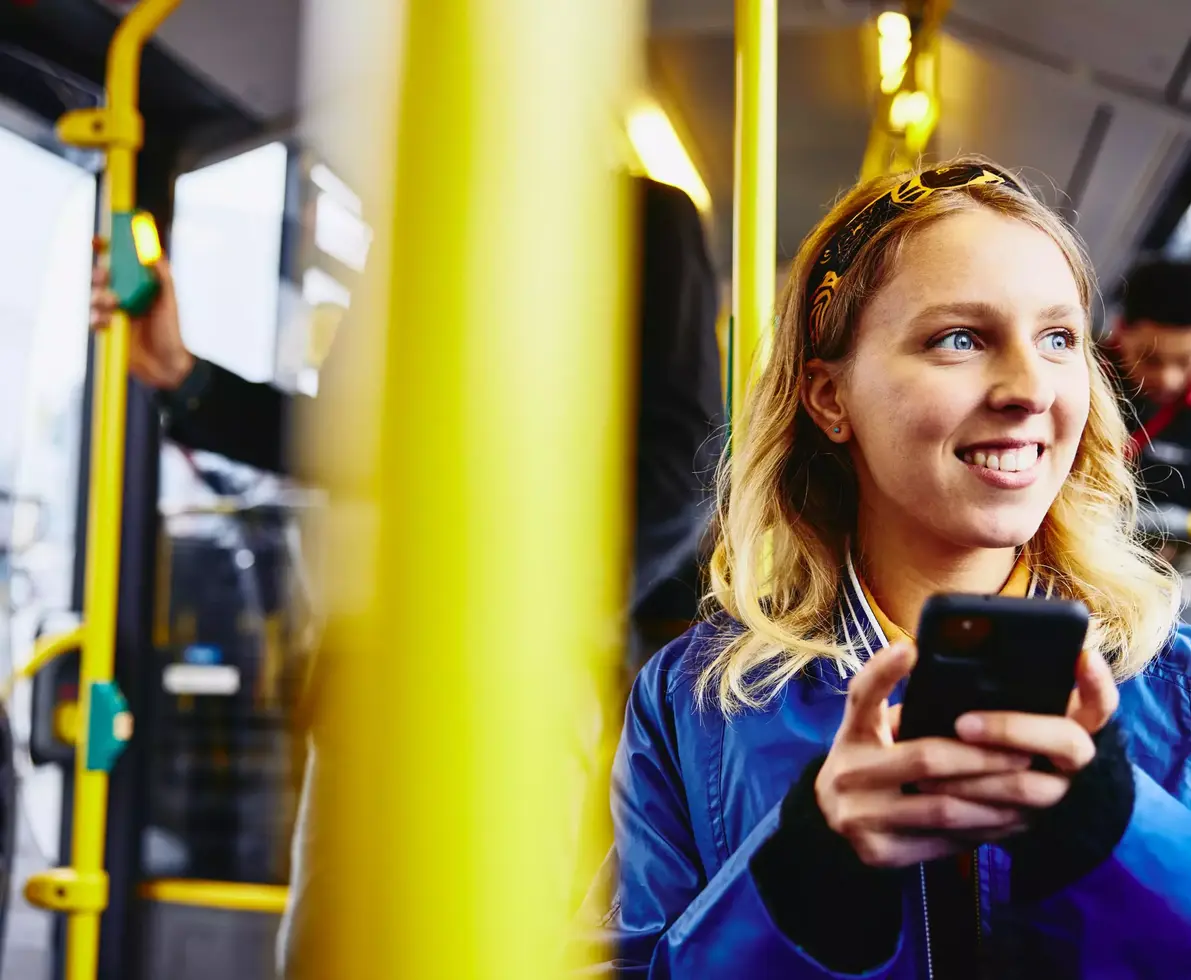 Smiling female, looking outside while holding her phone and sitting in the bus.
