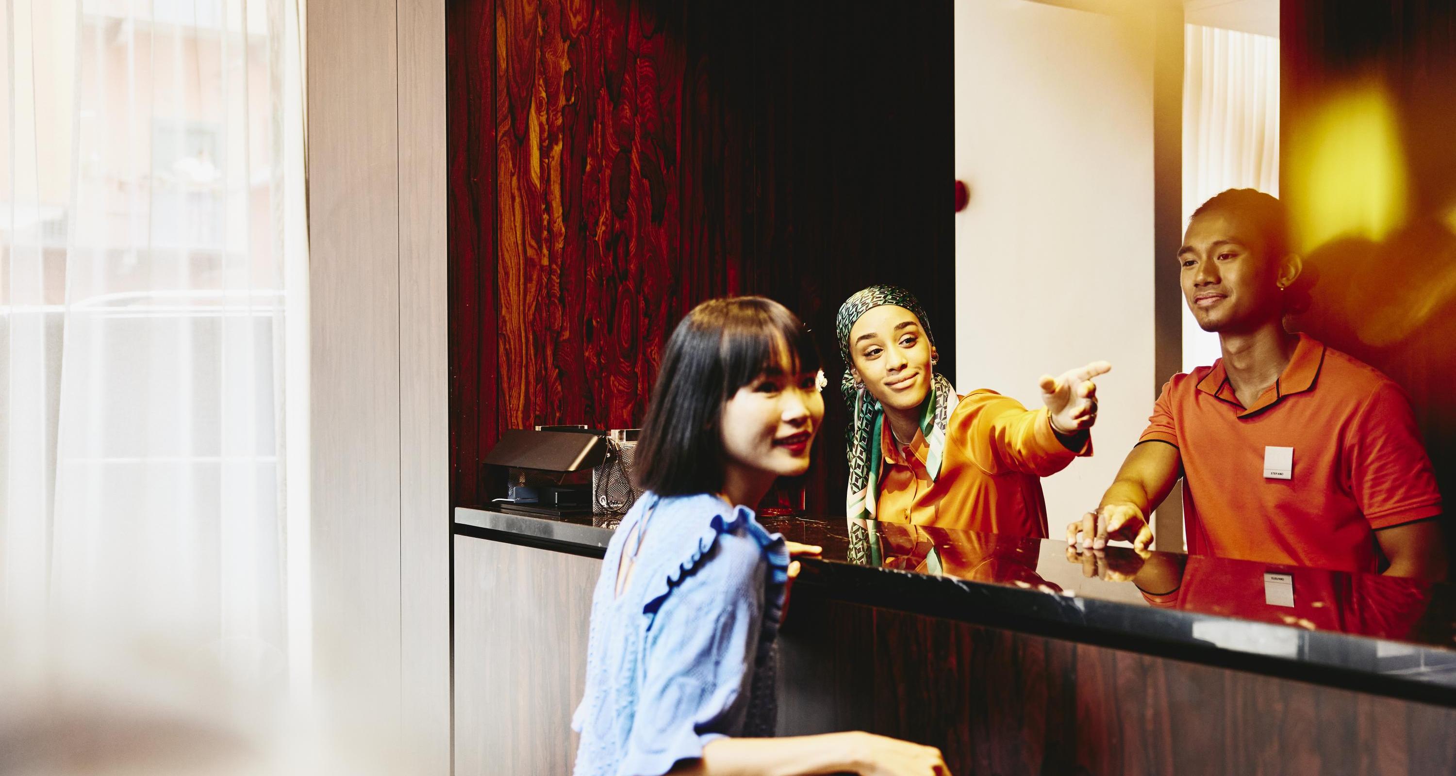 Man and woman working at a hotel reception desk helping a guest.