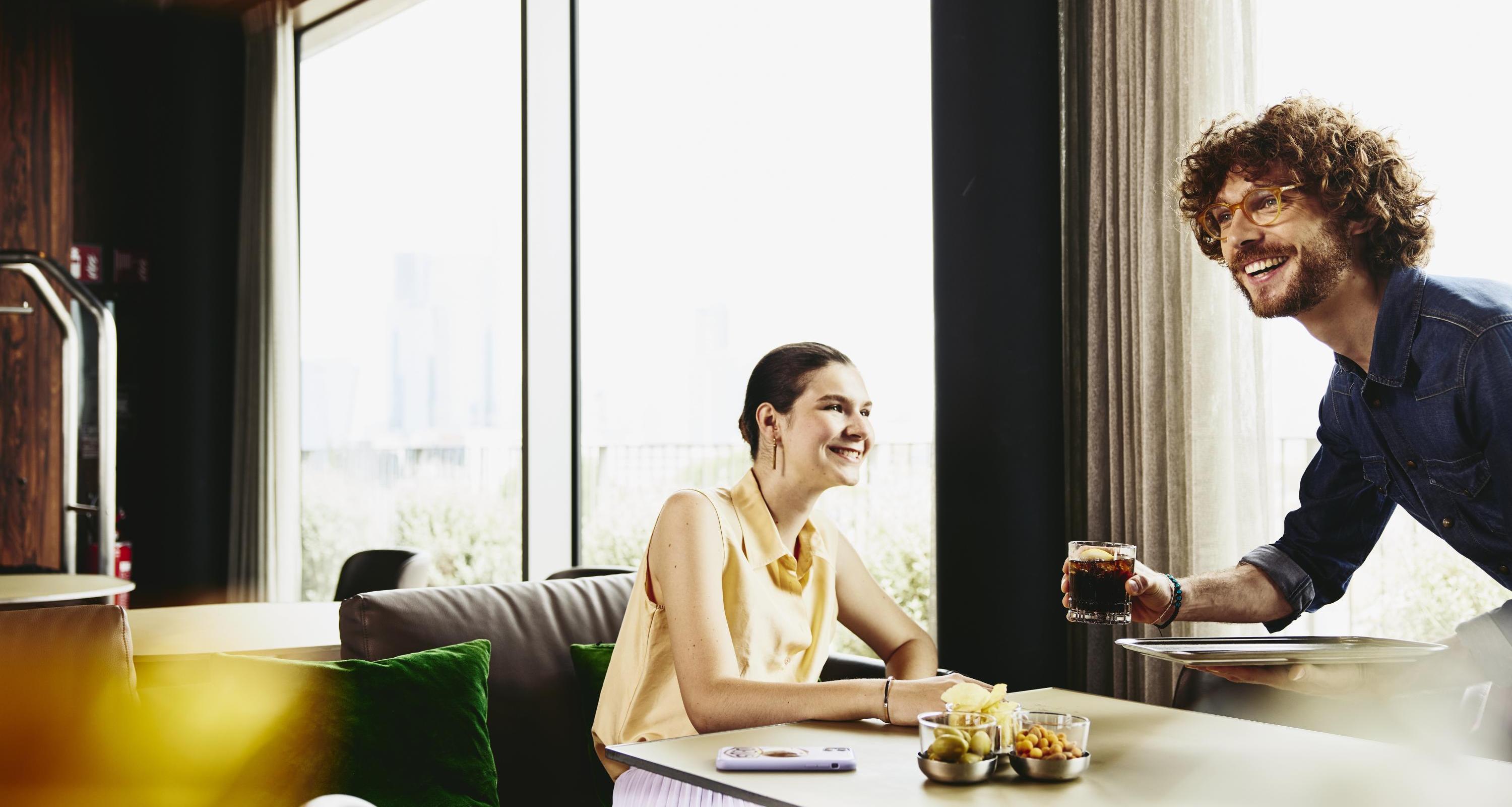 Waiter serving a drink to woman sitting at a table.