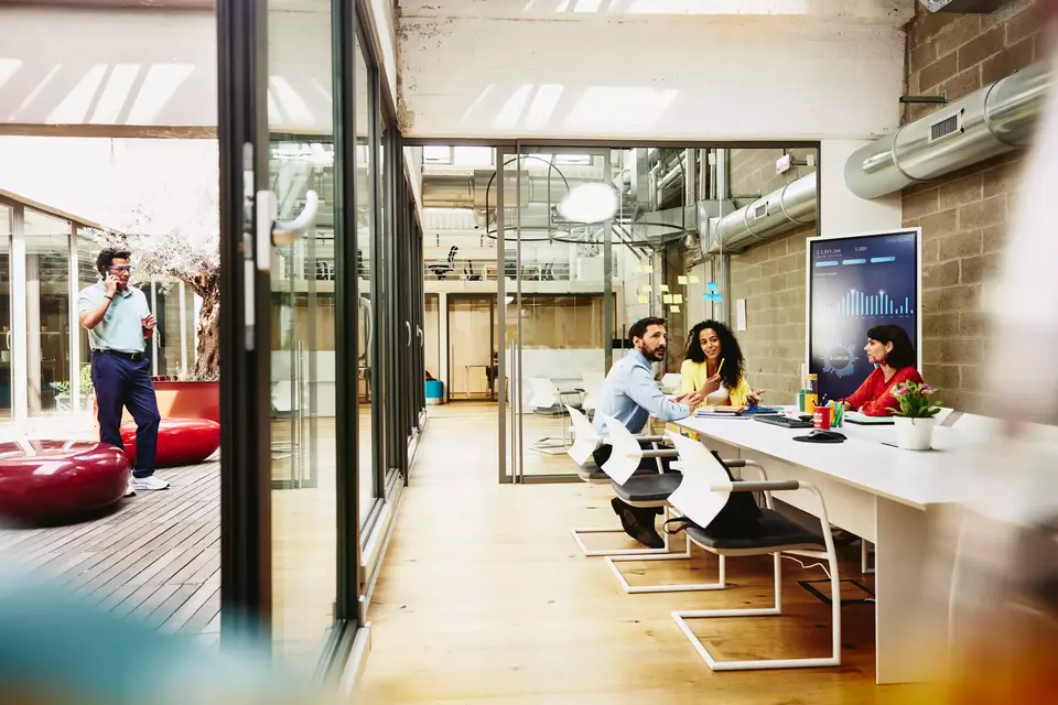 Three colleagues having a meeting in a meeting room, while one colleague is making a call outside the room.
