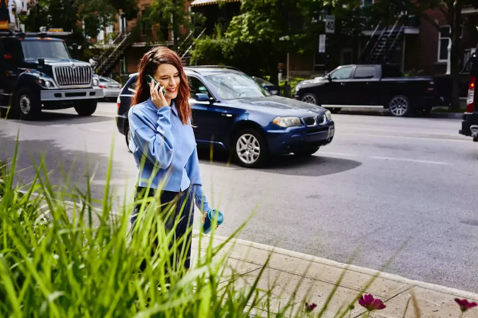 Female, talking on mobile phone, walking on sidewalk in busy street
