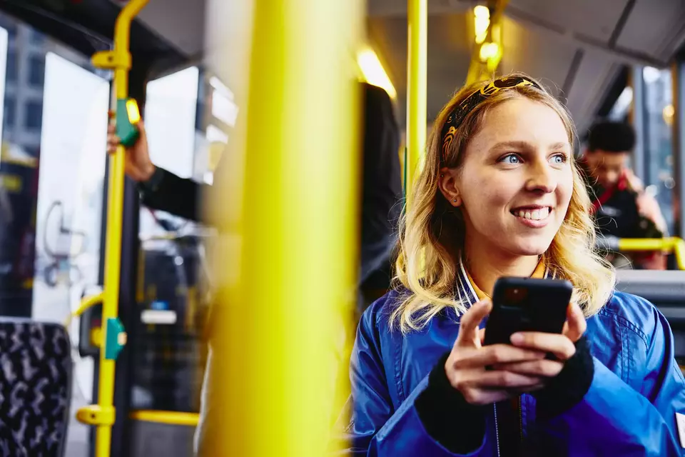 Smiling female, looking outside while holding her phone and sitting in the bus.
