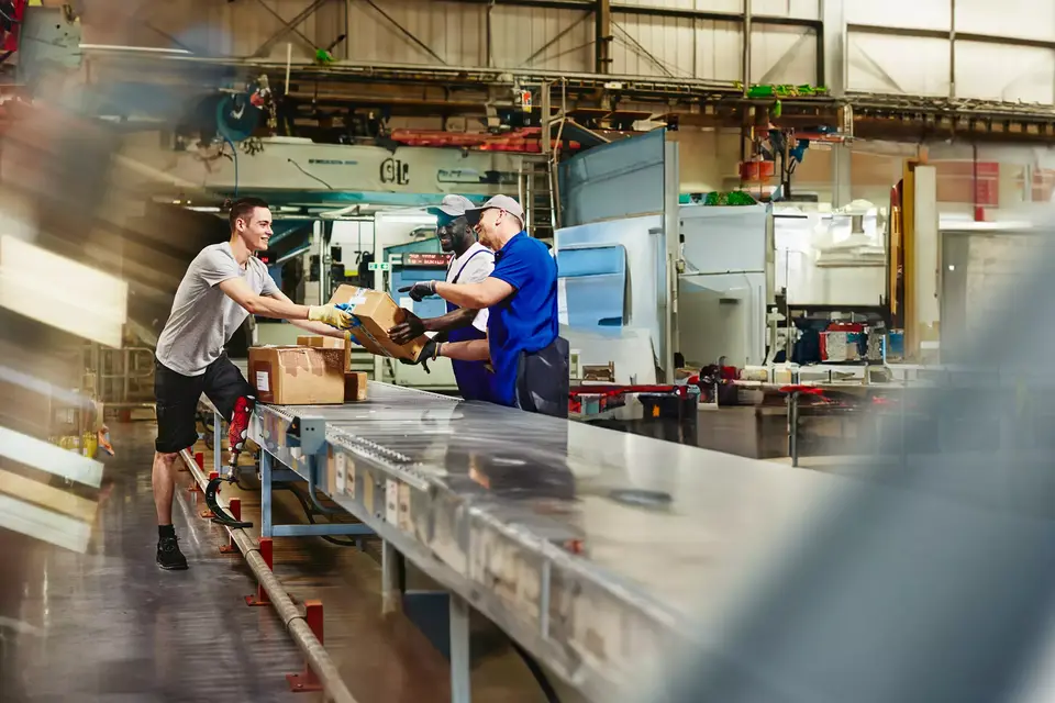 Three people working next to an assembly line with packages. 
