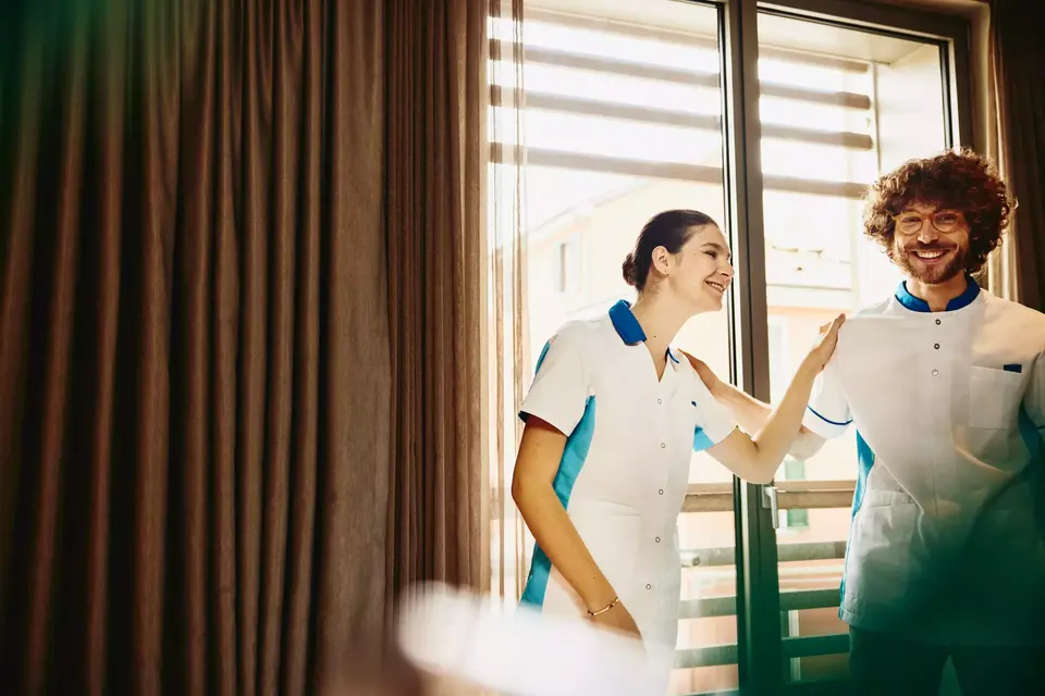 Two colleagues smiling, working housekeeping in a hotel room.
