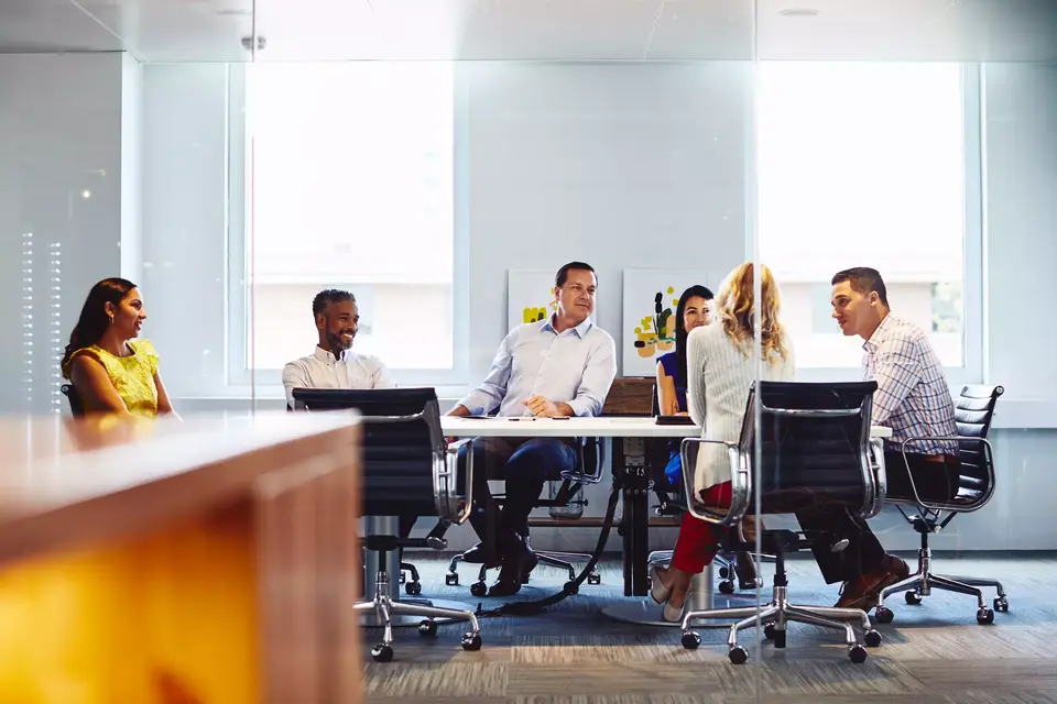 Group of colleagues sitting down in a meeting room at the office, smiling.
