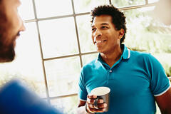 Smiling male holding a coffee cup having a chat with someone.